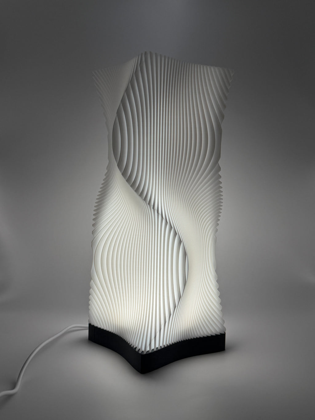 Moderne weiße Lampe mit 3D-gedruckter, wellenförmiger Lamellenstruktur, die ein indirektes Licht  wirft.