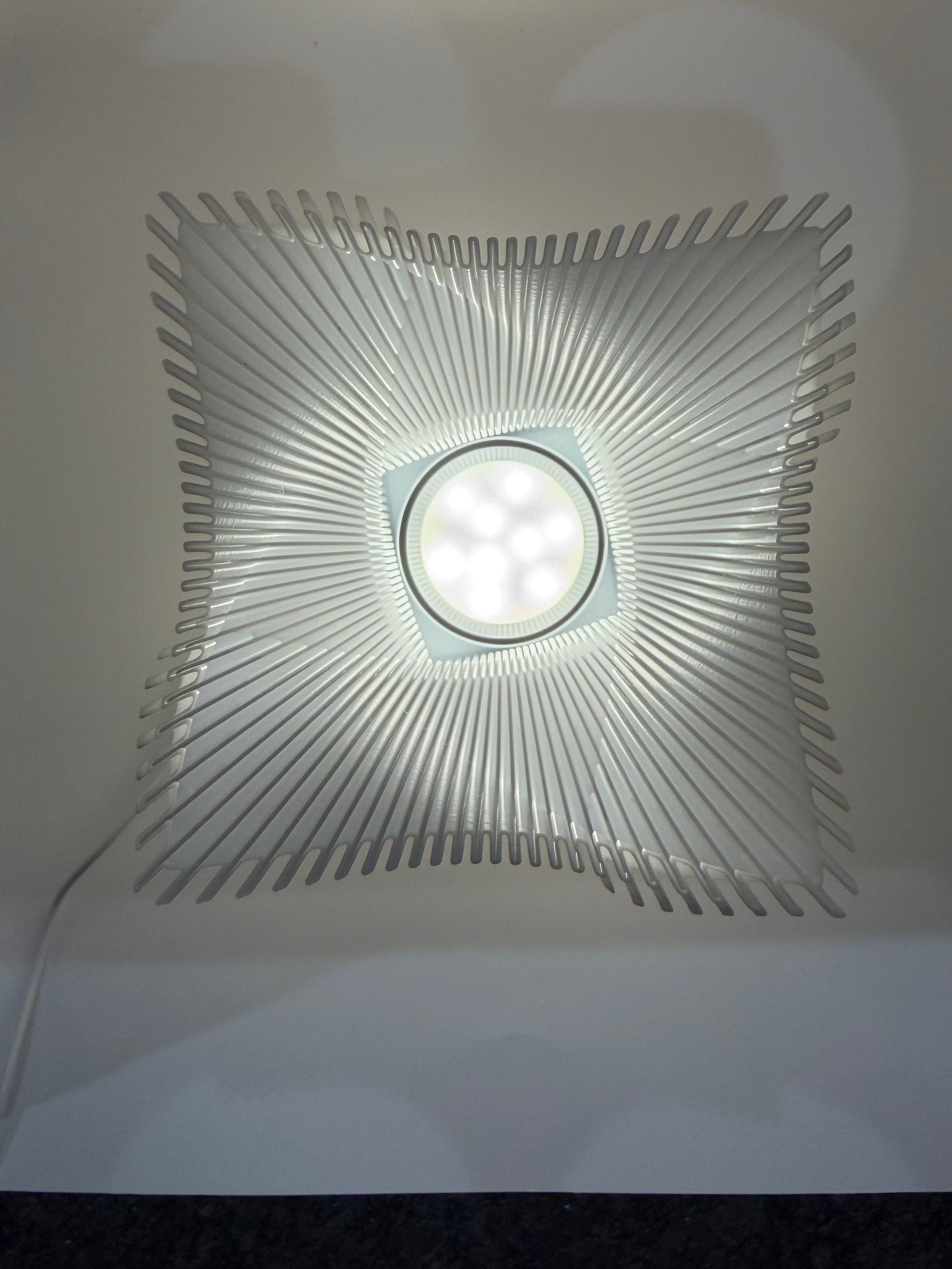 Moderne weiße Lampe mit 3D-gedruckter, wellenförmiger Lamellenstruktur, mit sicht auf die LED-Leuchte.